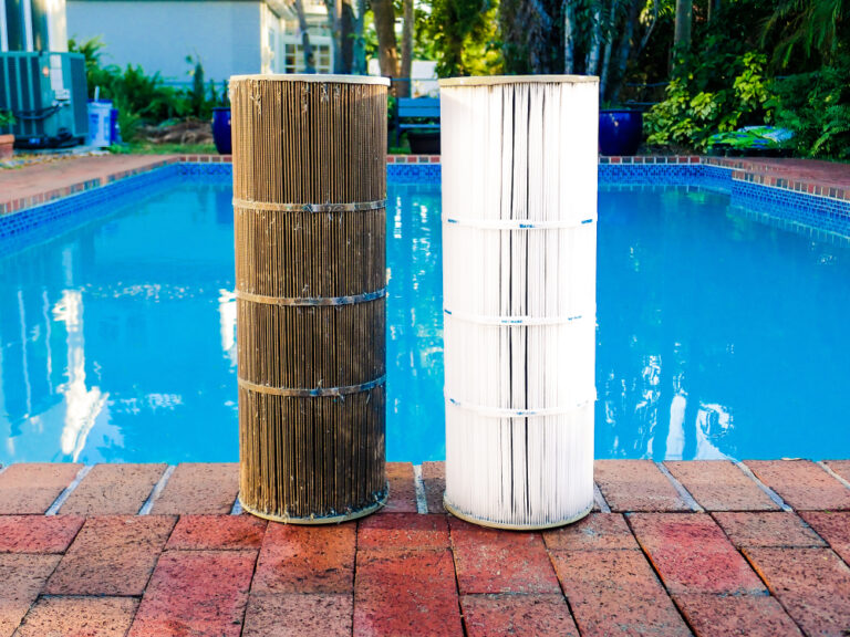 Juxtaposition of a dirty reusable washable pleated reinforced polyester cartridge pool filter next to a clean filter, after routine maintenance cleaning. Pool surrounded by bricks in background.
