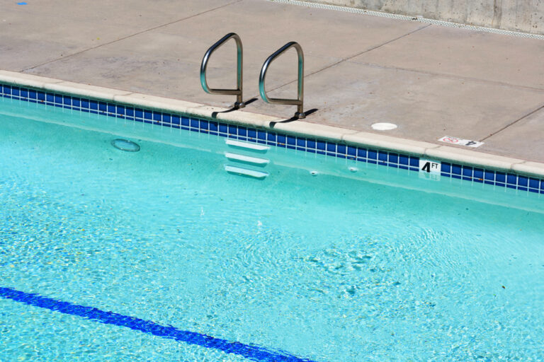 Blog 4 Elevated view of the outdoor swimming pool with metal handrails and steps, depth marker on the pool edge, underwater light fixture and blue line on the bottom of the pool
